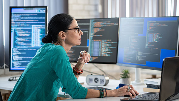 Person at workstation with multiple monitors running code.